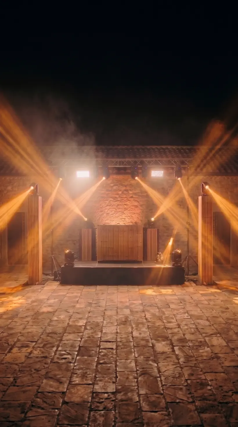 Patio de noche con dos columnas de madera iluminadas a los lados de la cabina y haces ámbar cruzando la pista vacía